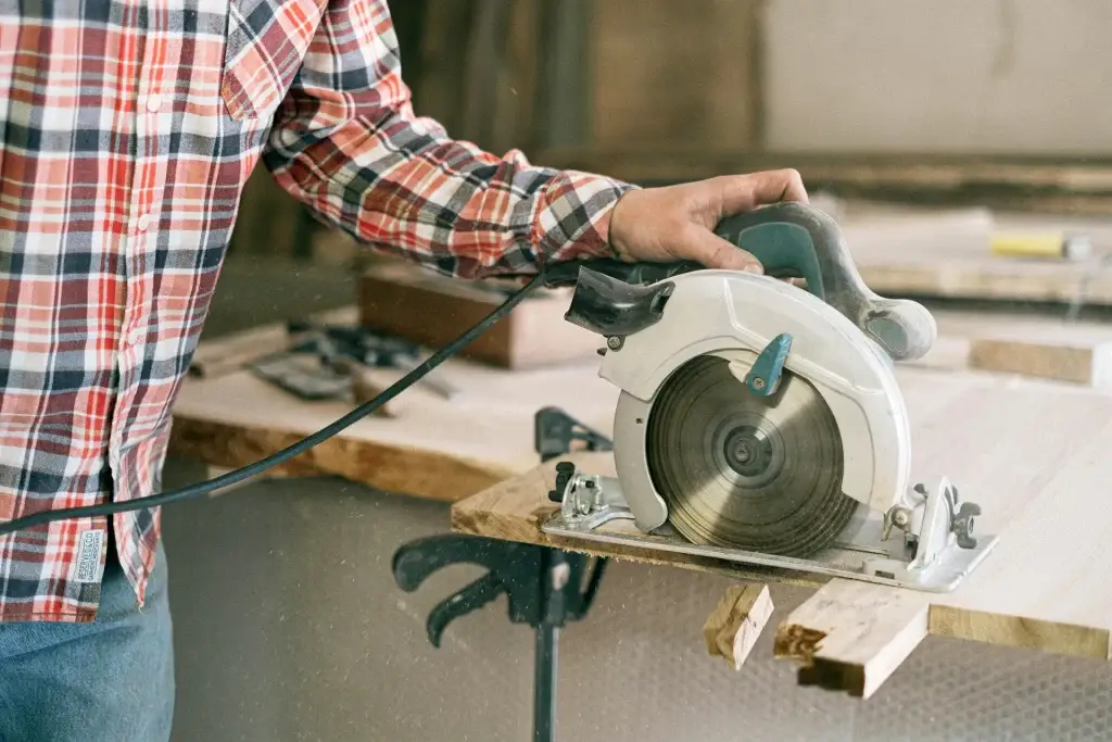 Charpentier en chemise à carreaux utilisant une scie circulaire pour couper une planche de bois dans un atelier de construction.