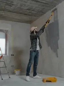 Un entrepreneur général de Construction HERA appliquant de la peinture grise sur un mur intérieur à l’aide d’un rouleau télescopique.