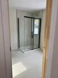 Douche vitrée à cadre noir installée dans une salle de bain rénovée – Construction HERA