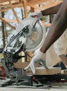 Charpentier effectuant une coupe de bois avec une scie à onglet sur un chantier – Construction HERA